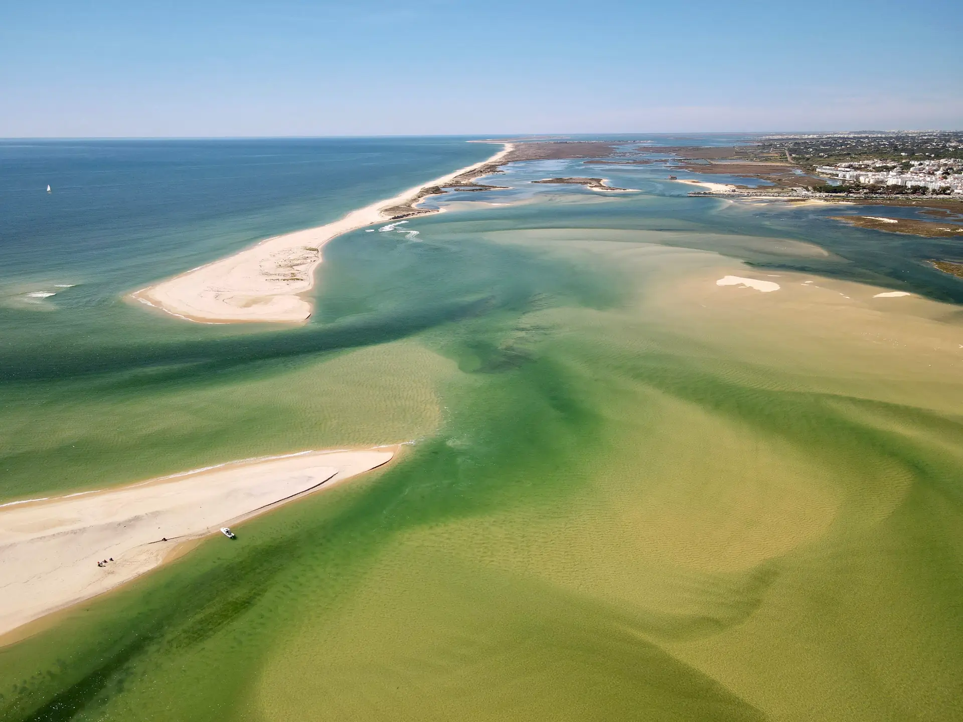 Aerial view of the Ria Formosa: white barrier-island sandbanks, green shallow channels and the open sea beyond