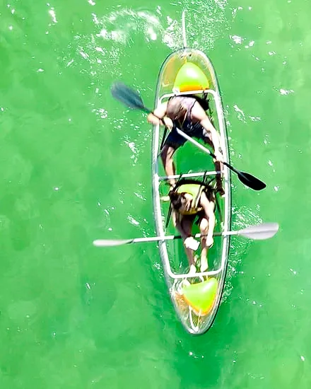 Two paddlers from above in a clear kayak over bright green shallow water