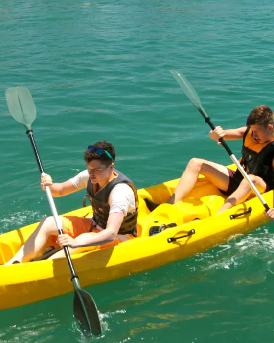 Two paddlers in a yellow double sit-on-top kayak on turquoise lagoon water